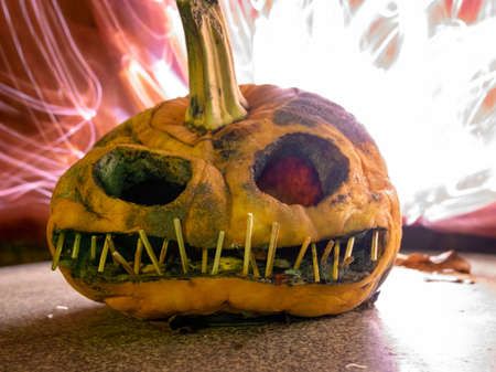 terrible a burning carved pumpkin with a scary face and colorful light drawings in a dark background, suitable for Halloweenの写真素材