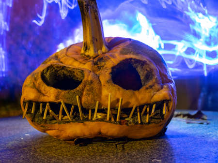 terrible a burning carved pumpkin with a scary face and colorful light drawings in a dark background, suitable for Halloweenの写真素材