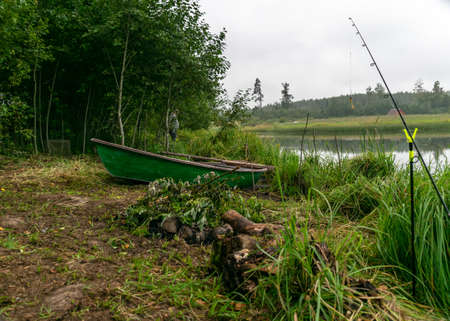 landscape with lake shore and fisherman's accessories, calm lake water surface, tree reflections, cloudy day, fishing conceptの写真素材