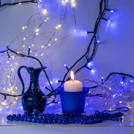 blue composition with candle and miniature mug, blue pearl ornaments in the foreground, white and blue light chain background, Christmas waiting time, winter timeの写真素材