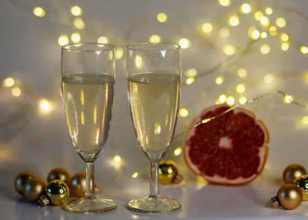 two glasses of champagne, pink grapefruit, golden glass balls and various Christmas decorations, illuminated background of a chain of white lights, Christmas waiting time, winterの写真素材