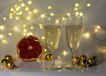 two glasses of champagne, pink grapefruit, golden glass balls and various Christmas decorations, illuminated background of a chain of white lights, Christmas waiting time, winterの写真素材