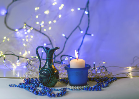 blue composition with candle and miniature mug, blue pearl ornaments in the foreground, white and blue light chain background, Christmas waiting time, winter timeの写真素材