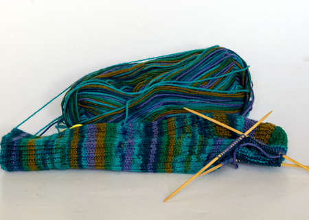 knitted sock knitted with green striped yarn, wooden knitting needles and a ball of wool yarn, handicrafts as a hobby, knitting concept, handicraftの写真素材