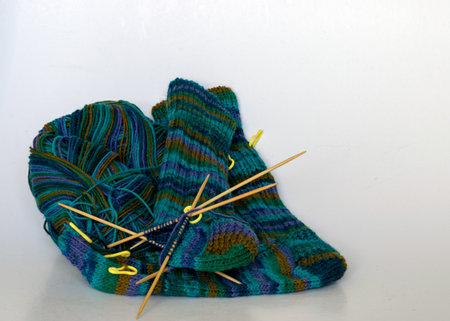 knitted sock knitted with green striped yarn, wooden knitting needles and a ball of wool yarn, handicrafts as a hobby, knitting concept, handicraftの写真素材