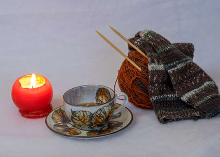 colorful and variegated knit socks with knitting needles, yarn ball and tea cup, red burning candle,...