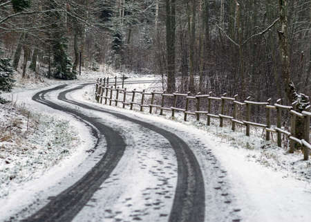 winter landscape with snowy road, snow-covered wooden fence, trees and shrubs by the road, winter dayの写真素材