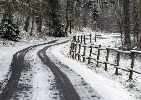 winter landscape with snowy road, snow-covered wooden fence, trees and shrubs by the road, winter dayの写真素材