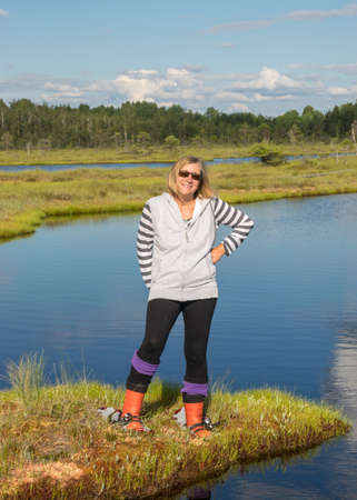 beautiful swamp landscape with blue sky and water, woman enjoys swamp landscape, hike with snowshoes in swamp, traditional swamp plants, mosses and trees, bog in summerの写真素材