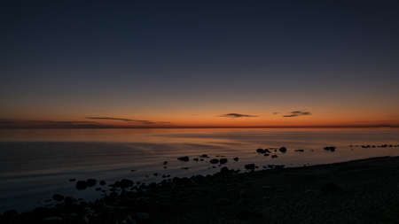 orange sunset by the sea, black stone silhouettes against the sea background, summer eveningの写真素材