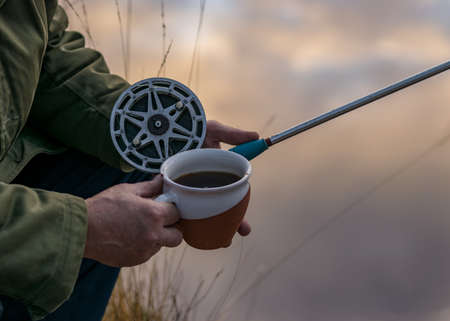 close-up view with fisherman's hands, fishing reel and tea cup on a blurred background, fishing in autumn, autumnの写真素材