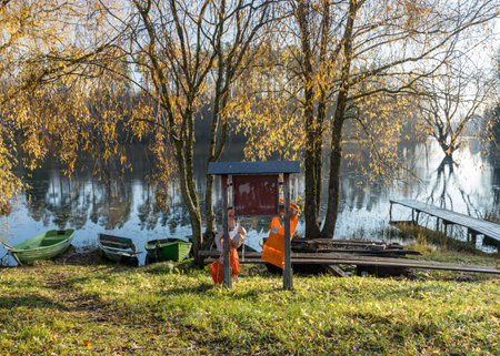 bright autumn landscape with lake shore, yellow birch branches, boats and information board with bright life jackets, fishing conceptの写真素材