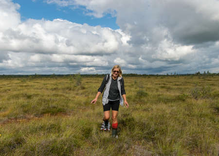 summer landscape in the swamp, a woman walks through the swamp with swamp shoes and orange rubber boots on her feetの写真素材