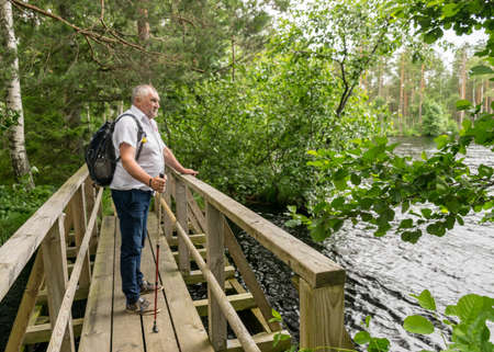 landscape with a man in a white shirt by the bog lake, wooden bridge, strong wind in the trees and thrilled lake water, summer in the bogの写真素材
