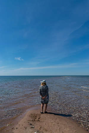 a female figure on the seashore, a beautiful blue sky and a white pebble beachの写真素材