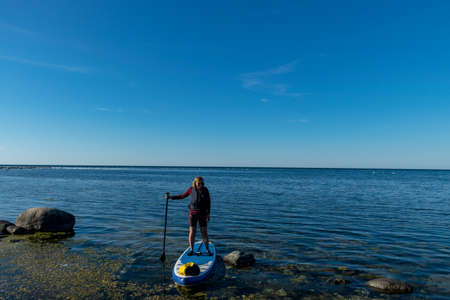 seascape with woman on paddle board, calm blue sea and skyの写真素材