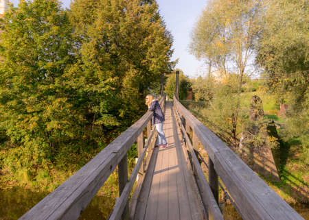 picture with a wooden bridge over the river, a silhouette of a woman on the bridge, trees and shrubs in the backgroundの写真素材