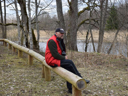 figure of a sitting man on a wooden fence on the river bank, spring timeの写真素材