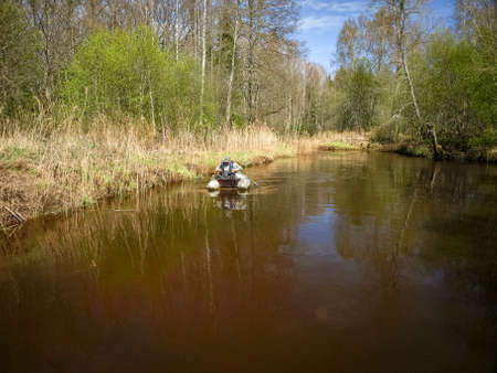 small wild river landscape, first spring greenery, fisherman's silhouette in a boat, reflections in the river waterの写真素材