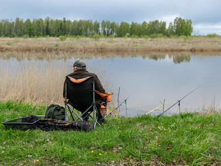 spring landscape with a fisherman on the shore of the lake, fishing accessories in the green hall are in the foregroundの写真素材