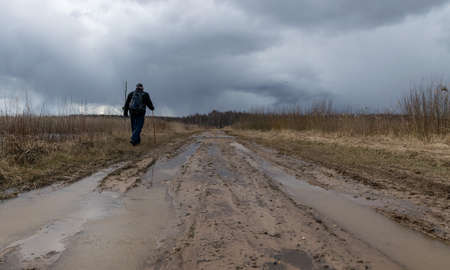 landscape with a human figure on a dirty dirt road, old reeds on the side of the road, spring viewの写真素材