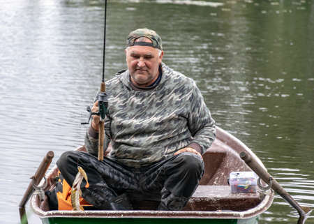 landscape with a fisherman in a boat, a small pike attached to the fisherman, a calm lake water surface, tree reflections, a cloudy day, fishing conceptの写真素材