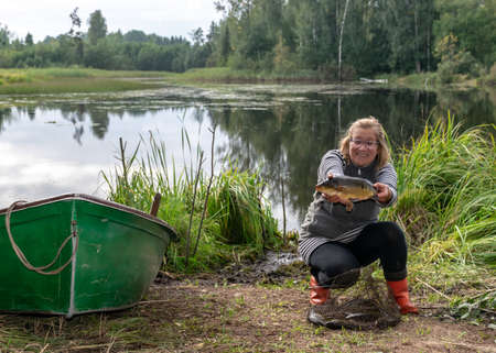 photography with a fisherman who is happy, she shows her fish, the concept of fishing, fishing as a hobby, outdoor recreationの写真素材