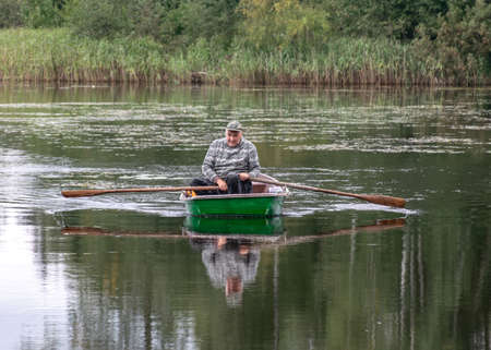 landscape with a fisherman in a boat, calm lake water surface, tree reflections, cloudy day, fishing conceptの写真素材