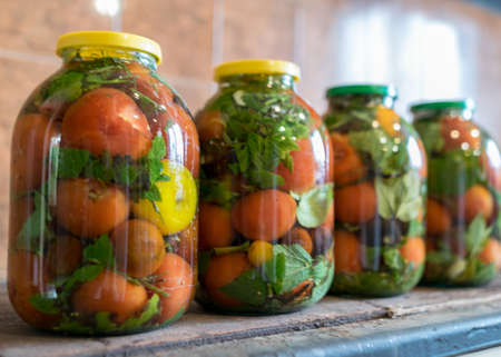 photography with red tomatoes and green spices in glass jars, canned vegetables, tomato pickling, winter products, healthy diet, vegetarian diet, autumn harvest timeの写真素材