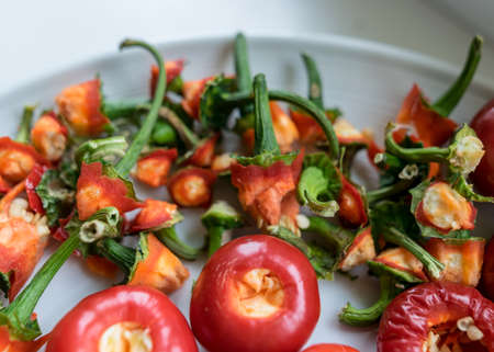 picture with tomato peppers on a white plate, peppers prepared for canning, green stalks separated, concept of healthy eating, vegetarian diet, canning products for winter, autumn harvest timeの写真素材