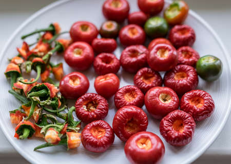 picture with tomato peppers on a white plate, peppers prepared for canning, green stalks separated, concept of healthy eating, vegetarian diet, canning products for winter, autumn harvest timeの写真素材