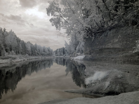 infrared surreal landscape with snowy trees, reflections of clouds and trees in the water, photographed with a modified infrared camera, infrared photographyの写真素材