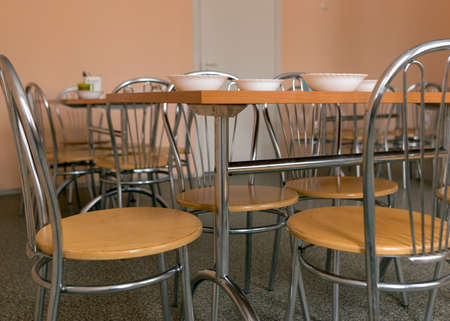 picture with tables and chairs in the school dining room, white bowls with lunch on the tableの写真素材