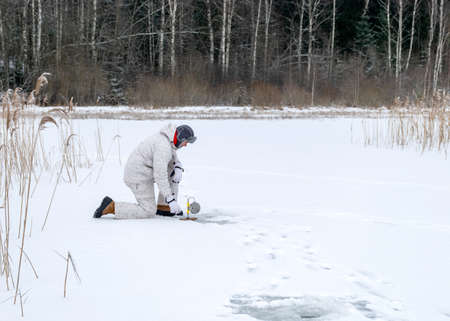 winter landscape on the river ice on a sunny day. winter sports, the angler enjoys ice fishing on the lake, winter fishing on the lake.の写真素材
