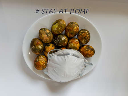 many bright and colorful Easter eggs with the words "stay home" and a face mask, an encouragement to protect yourself from the covid19 virusの写真素材