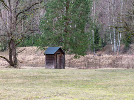 landscape with wooden toilet on the river bank, early spring, naked tree silhouettesの写真素材