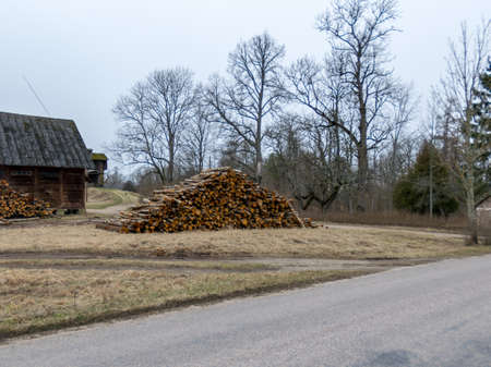 spring landscape with wooden barn and tree logs by the roadside