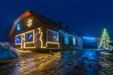 Night landscape with a decorated Christmas yard, light decorations, colored light reflections on a wet road in the foregroundの写真素材