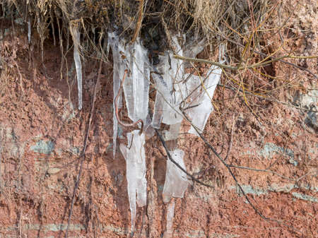photo with white ice icicles on the red clay walls, spring landscape of Vidzeme seashore, Latvia