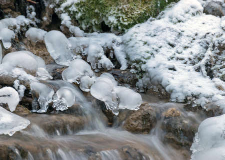 frozen fast flowing spring water, icy rocks and water stream, frosty tree roots, beautiful ice and...