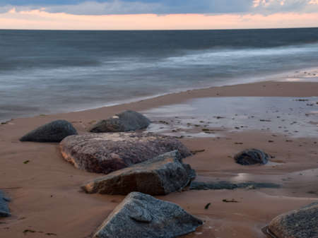 beautiful sunset scenery on a rocky beach, blurred waves and rocks in the foregroundの写真素材