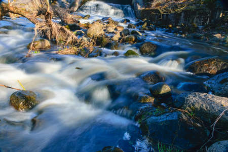 rapid river flow between rocks, water white as milk, long-term exposure, spring in nature