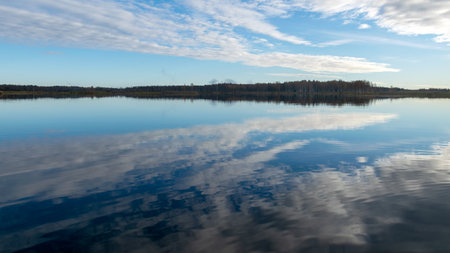 Beautiful lake at sunrise, golden hour sunrise, sunlight and grand cloud reflections on water, colorful dramatic sky at sunrise, dark silhouettes of trees, motion blurの写真素材