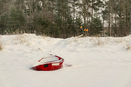 winter landscape from the seashore, red fisherman's boat on the seashore, sand and ice texture in...