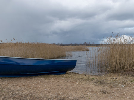 landscape with boats on the shore of the lake, dry reeds in the foreground, early springの写真素材