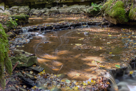 a small rapid river flows through dolomite rocks, long-term exposure, gentle and fuzzy river water, colorful autumn leaves and dry branches in the riverの写真素材