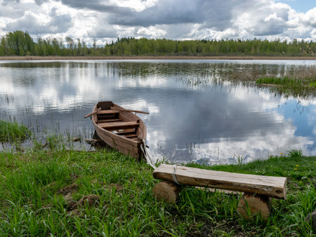 gorgeous spring landscape with calm lake water, wonderful cloud reflections in the lake water, a beautiful brown wooden boat on the lake shoreの写真素材