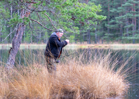 fisherman on the shore of a swamp lake, forest and swamp vegetation, rainy and cloudy autumn dayの写真素材