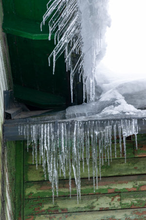 icicles are hanging from the roof, winter day, dangerous icicles on the roof of a house, icicles are...