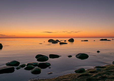 orange sunset by the sea, black stone silhouettes against the sea background, summer eveningの写真素材
